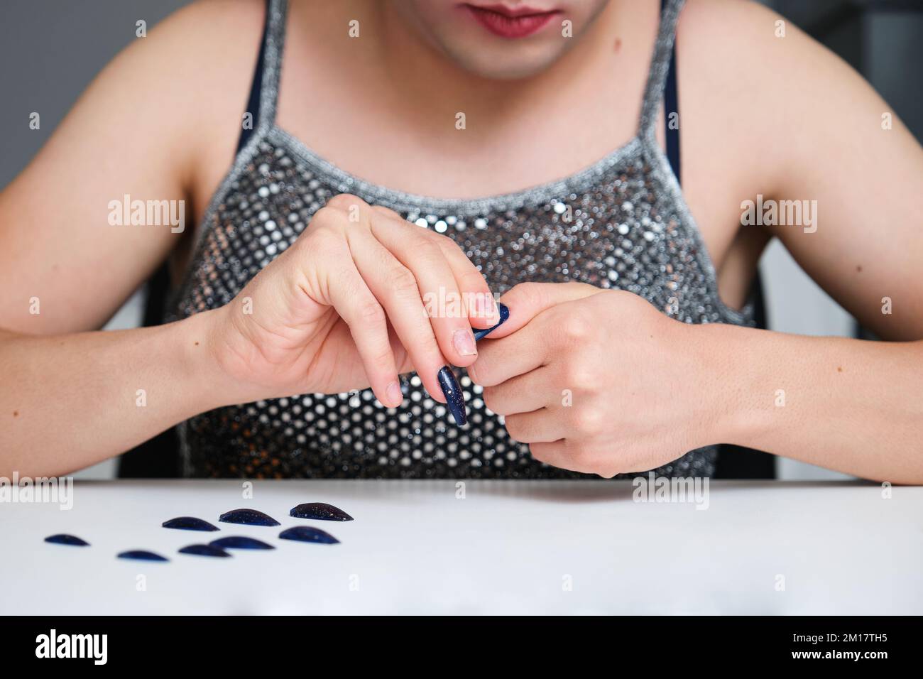 Giovane persona fluida di sesso irriconoscibile che rimuove le unghie false. Foto Stock