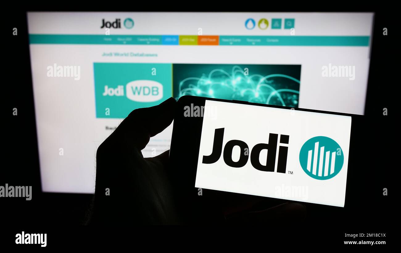 Persona che tiene il cellulare con il logo della Joint Organisations Data Initiative (JODI) sullo schermo davanti alla pagina web. Messa a fuoco sul display del telefono. Foto Stock