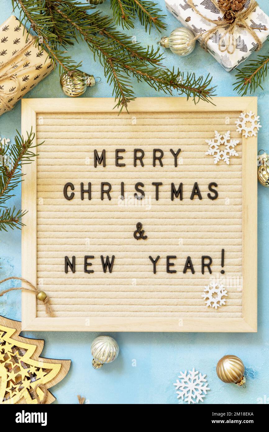 Allegra scritta di Natale sulla bacheca delle lettere, scatole dei regali e decorazioni d'oro su uno sfondo blu. Auguri di buon Natale e buone Feste NE Foto Stock