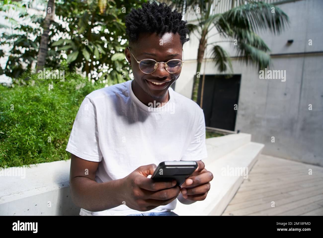 Ritratto di un uomo nero felice utilizzando un telefono cellulare e ridendo al campus universitario. Foto Stock