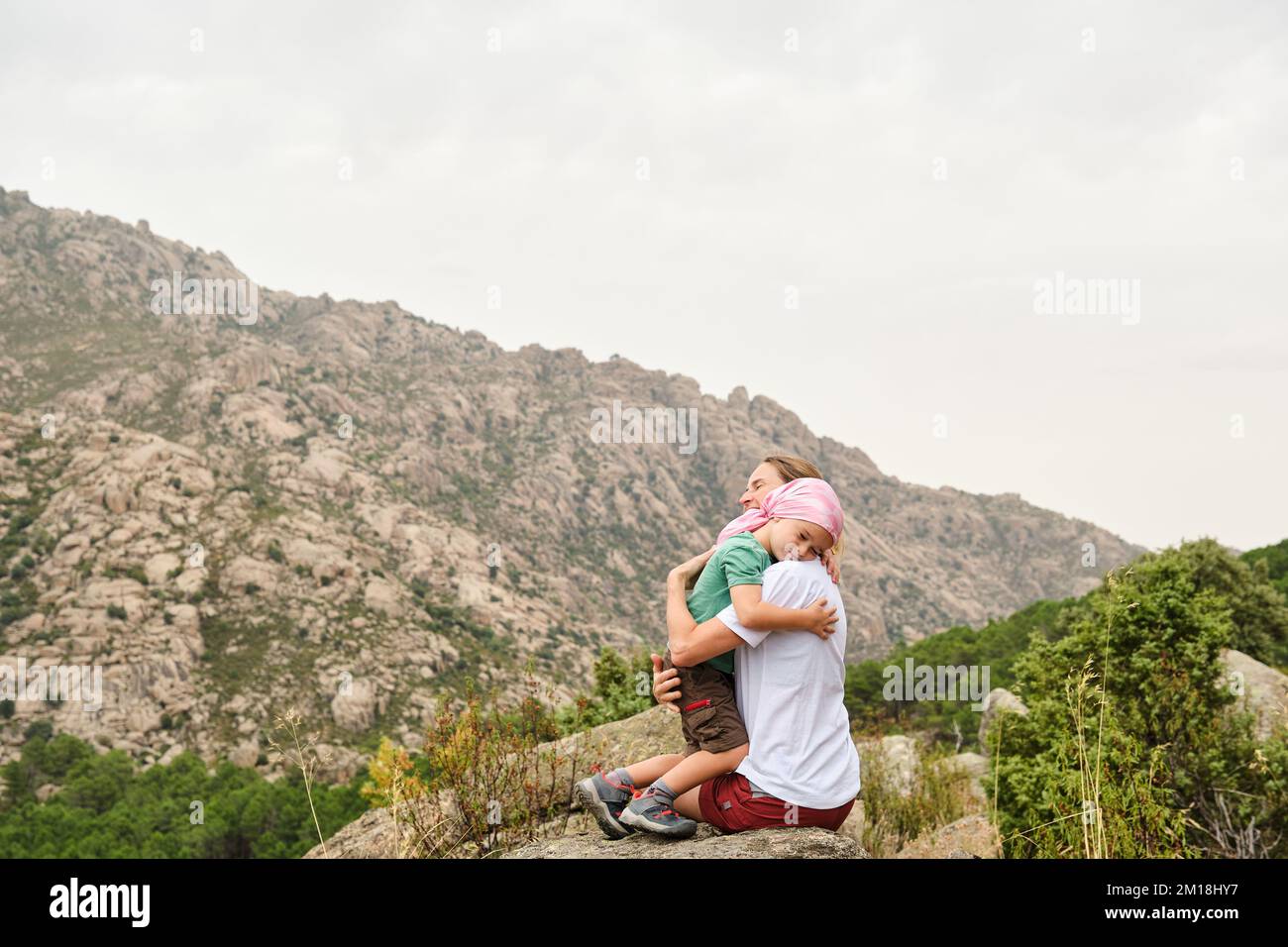Bambino con cancro che abbraccia sua madre in natura. Indossa una sciarpa rosa sulla testa Foto Stock
