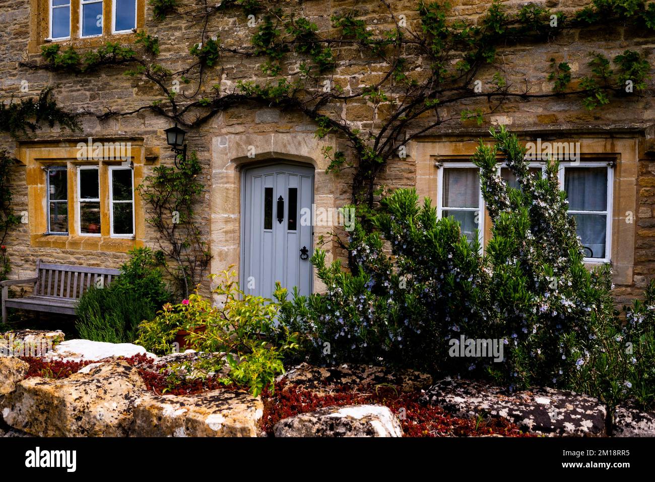 L'albero di Espalier, le finestre a trilioni e l'ingresso in pietra ad arco appuntito sono un'architettura da fiaba nel Lower Slaughter, Cotswolds District, Inghilterra. Foto Stock