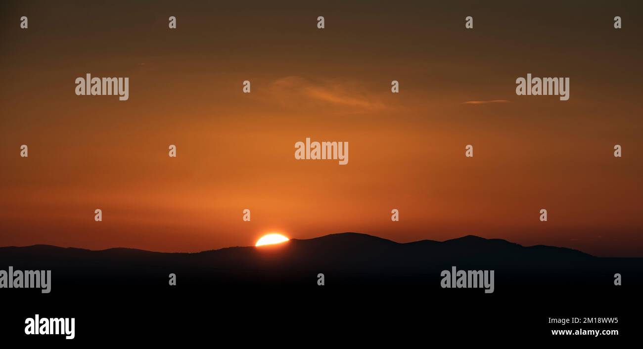 Il tramonto del sole invernale inizia a scendere sotto l'orizzonte delle famose Malvern Hills, Worcestershire, Inghilterra. Foto Stock