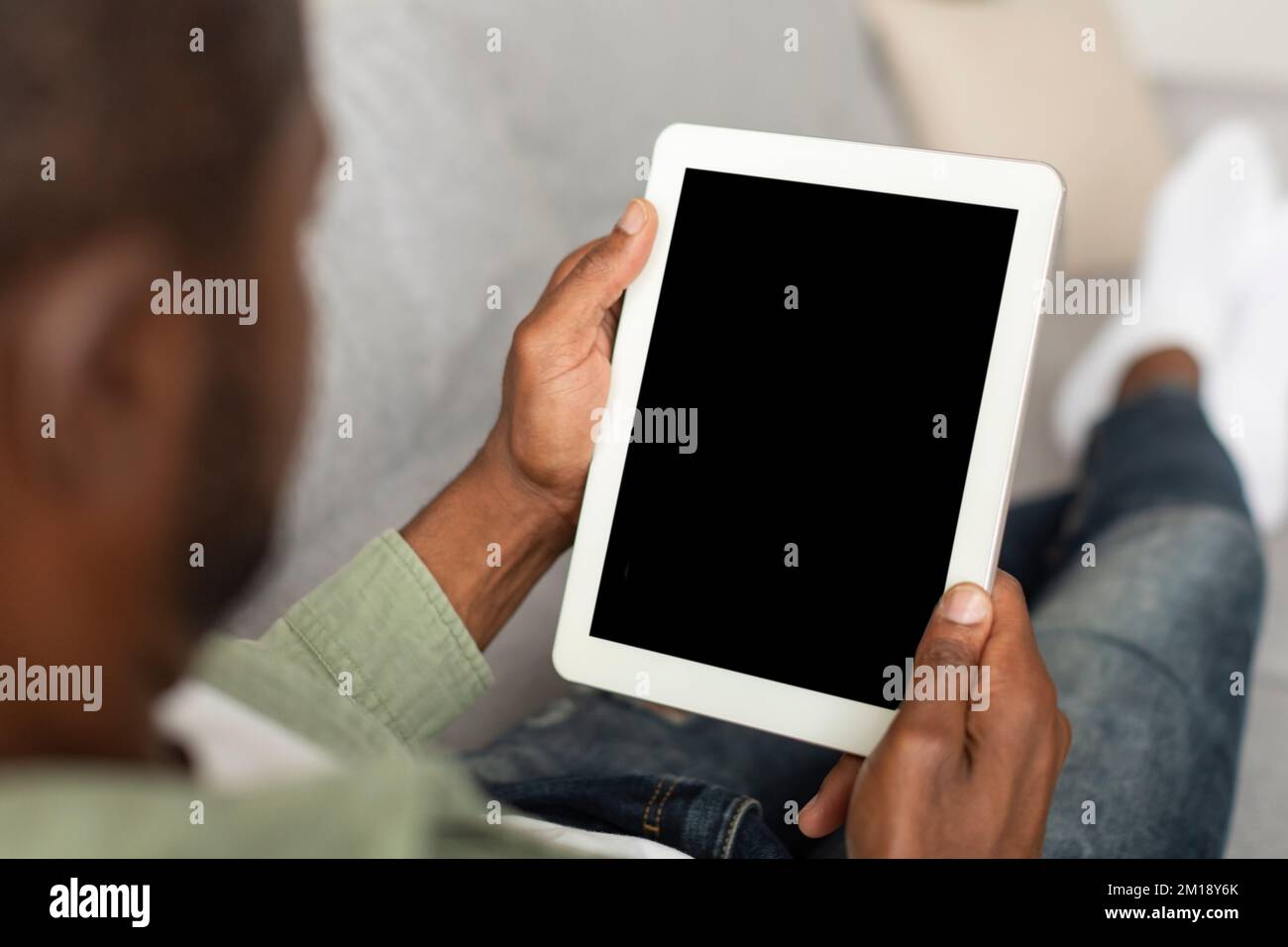 Uomo nero di mezza età che guarda il tablet con schermo vuoto utilizzando la nuova app per il lavoro e la chat in salotto Foto Stock