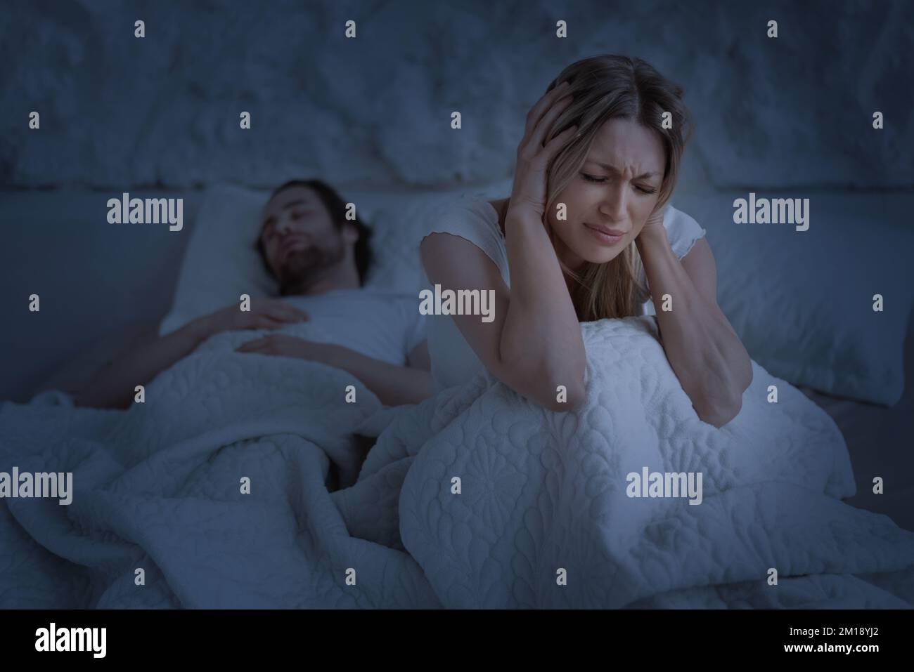 Donna depressa che soffre di russare il marito che dorme, donna che copre le orecchie con le mani, seduta sul letto nella notte Foto Stock