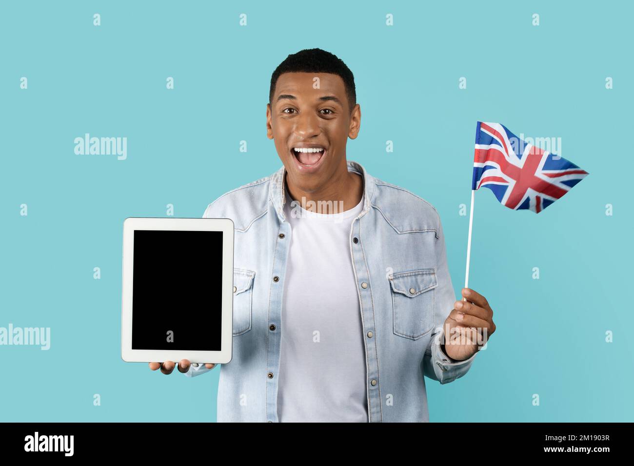 Allegro giovane afro americano studente con bocca aperta mostra bandiera Inghilterra, tablet con schermo vuoto Foto Stock