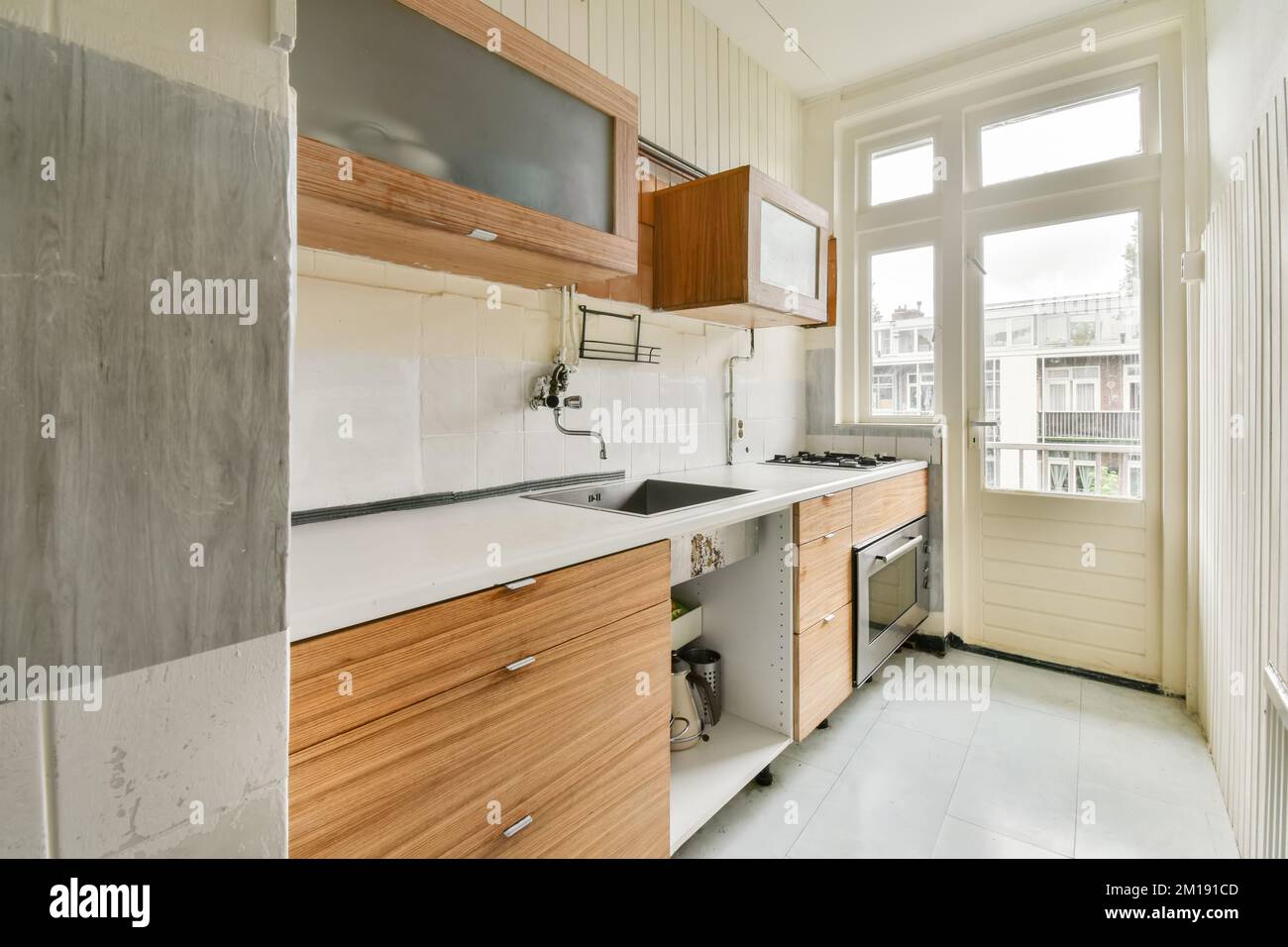 una cucina con armadi in legno e ripiani bianchi sul pavimento in una stanza vuota che è stata utilizzata per molti anni Foto Stock