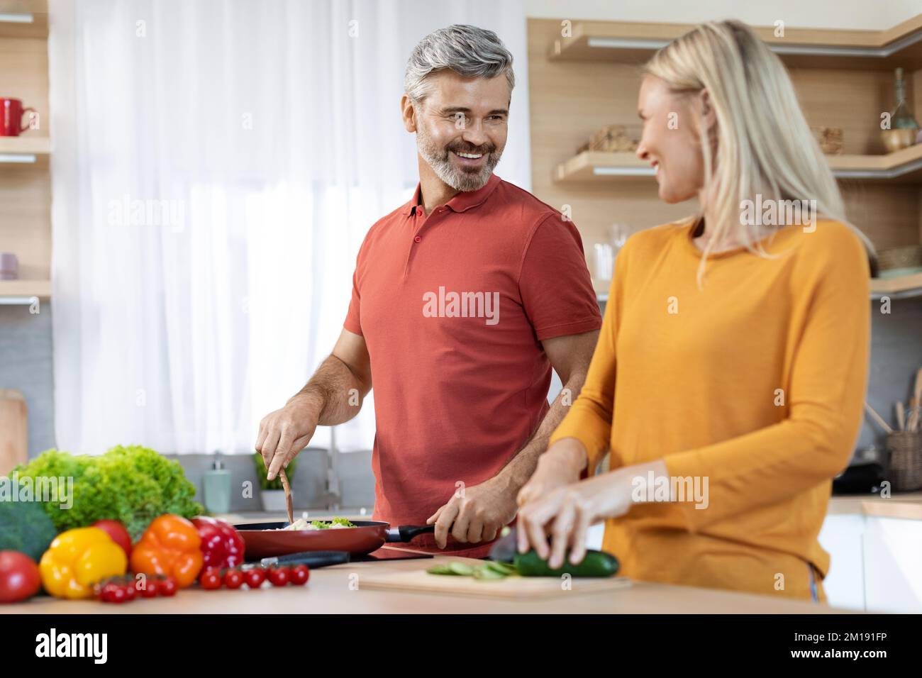 Sposi felici di mezza età che cucinano e che hanno conversazione, cucina interna Foto Stock