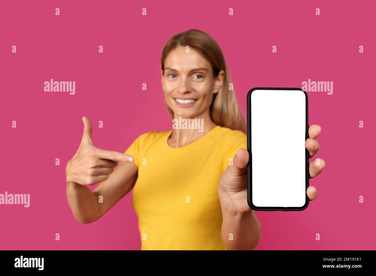 Felice adulta caucasica signora bionda in casual punta dito a smartphone con schermo vuoto, consiglia nuova app Foto Stock