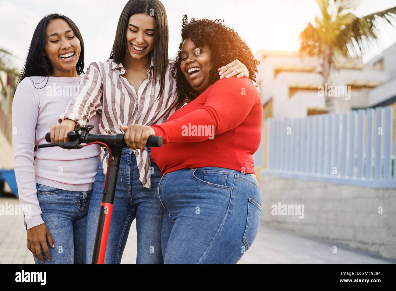 Ragazze multietniche felici che si divertono con scooter elettrico all'aperto - Focus sulla faccia ragazza africana Foto Stock