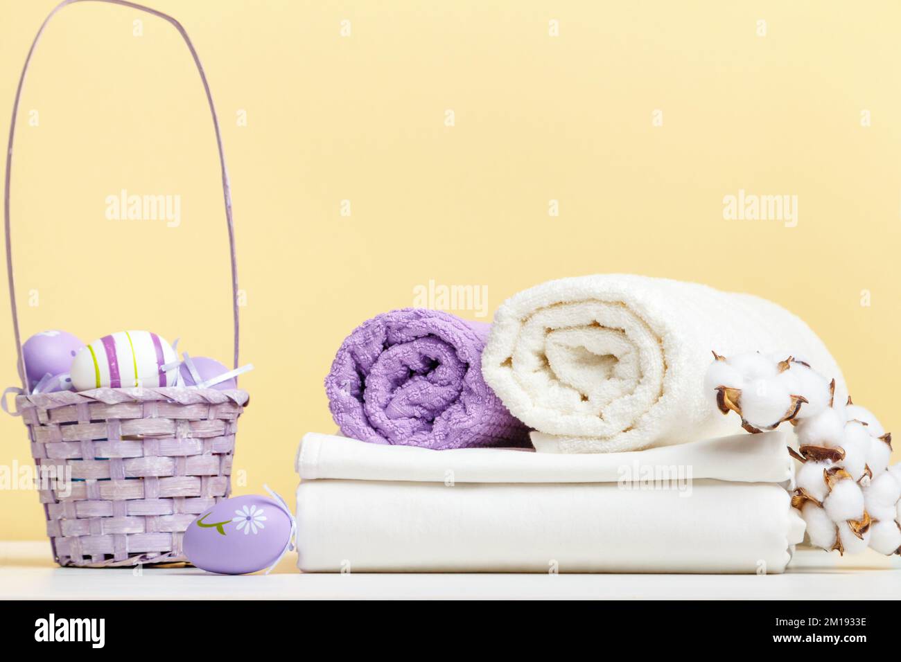 Biancheria da letto bianca ripiegata, rotoli di asciugamani cesto con uova di pasqua sul tavolo Foto Stock