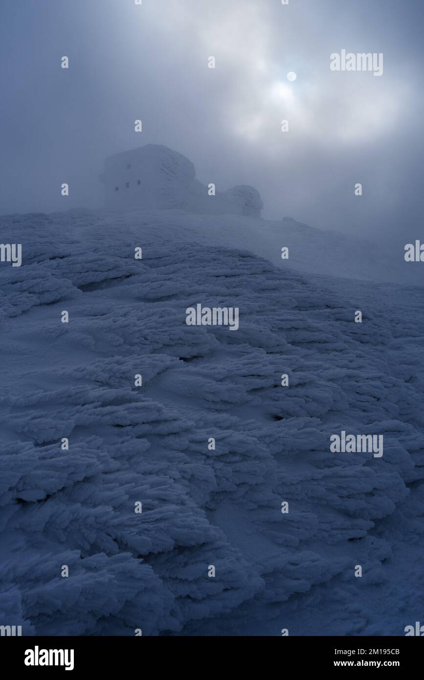 Clima invernale intenso con gelo e neve in montagna. Vecchio osservatorio nelle nuvole sulla cima di una montagna, Carpazi, Ucraina Foto Stock
