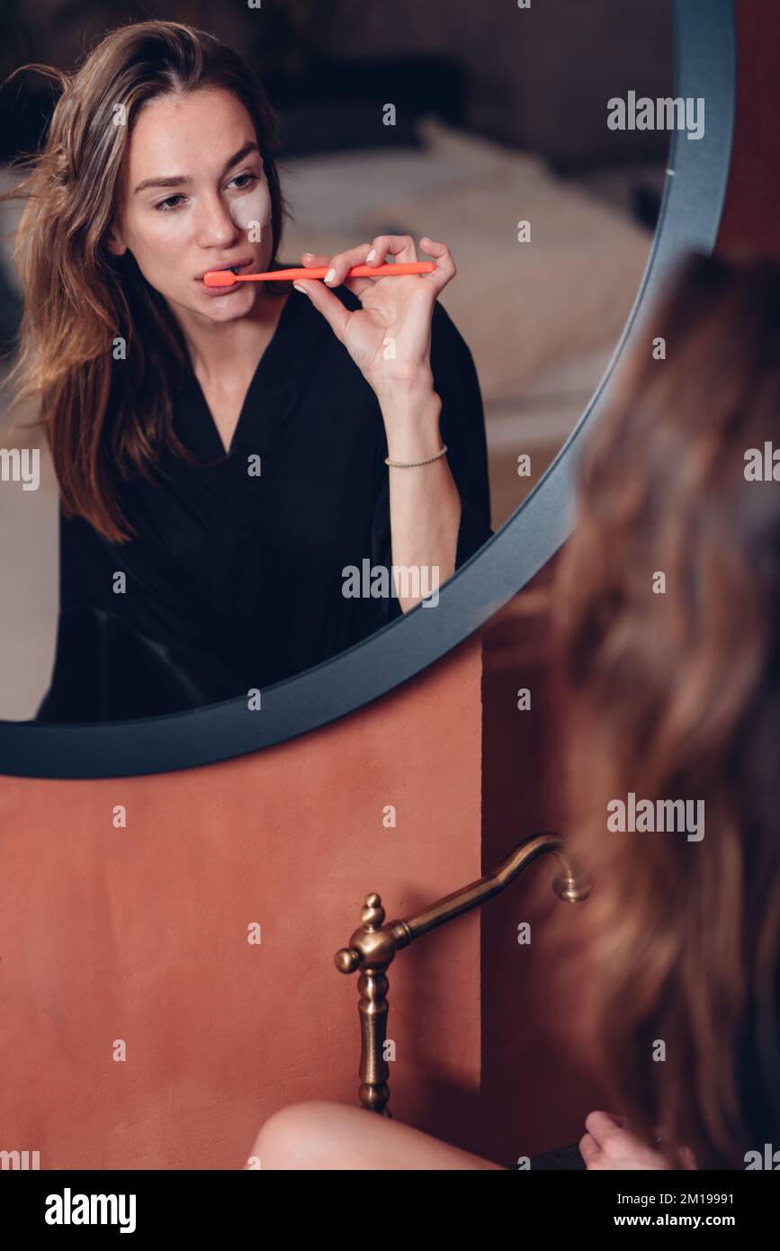 La giovane donna le sfiora i denti davanti allo specchio Foto Stock