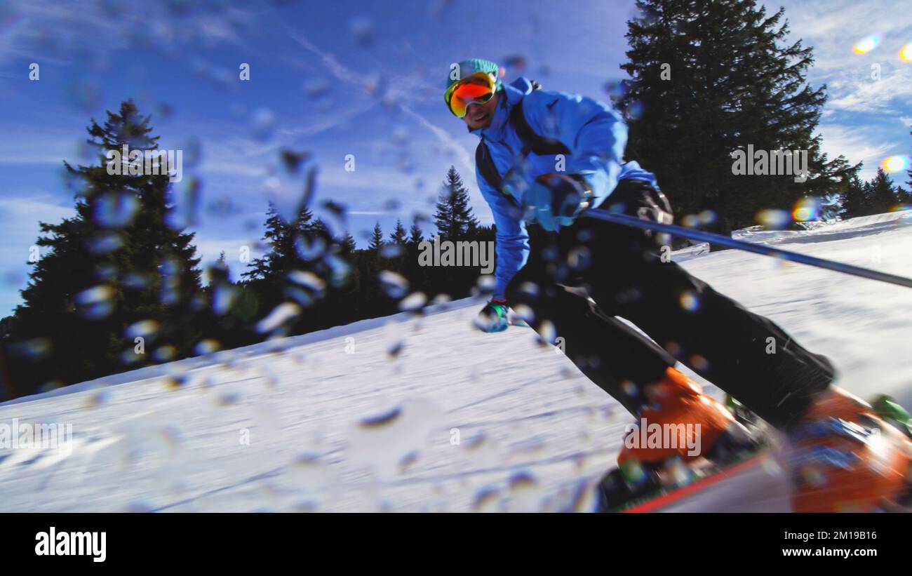 Sciatore professionista sulle piste delle alpi Svizzere e sciando la neve alla macchina fotografica. Gocce d'acqua visibili. Foto Stock