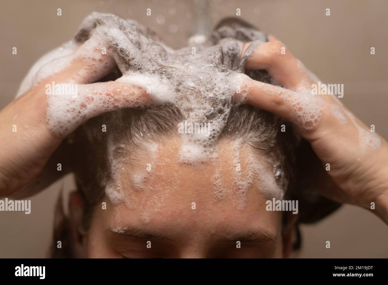 Closeup di una donna nei suoi trentenni lavando i capelli nella doccia e strofinando shampoo suts nei suoi capelli Foto Stock