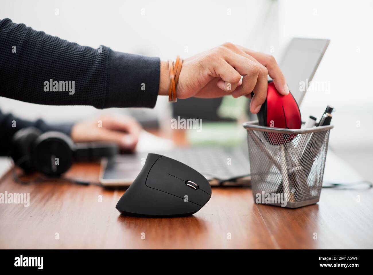 L'uomo che utilizza un mouse ottico verticale nero per computer dal design ergonomico e lascia il normale mouse per computer nel cestino. Foto Stock