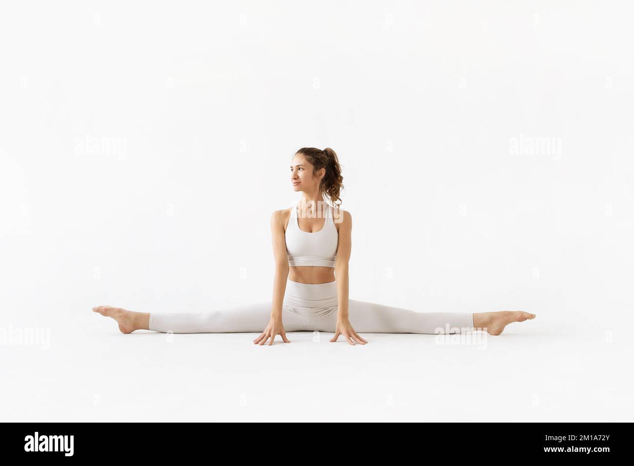 Una giovane donna che conduce uno stile di vita sano e pratica yoga, esegue l'esercizio samakonasana, spago trasversale, treni in bianco sportswear su un l Foto Stock