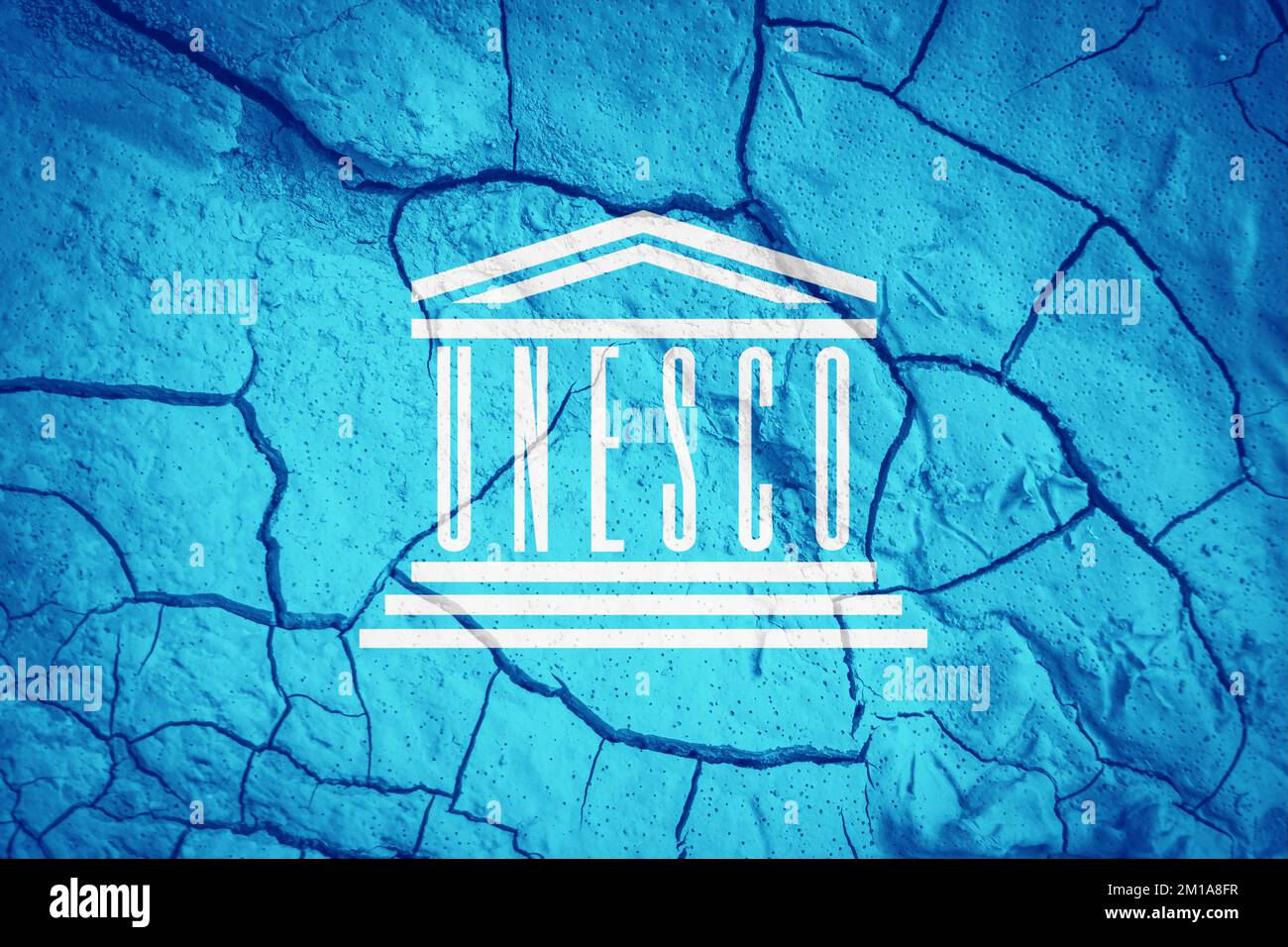 Bandiera delle Nazioni Unite dell'UNESCO. Bandiera delle Nazioni Unite. Simbolo dell'UNESCO. Bandiera sullo sfondo di terra secca spaccata. Bandiera con concetto di siccità Foto Stock