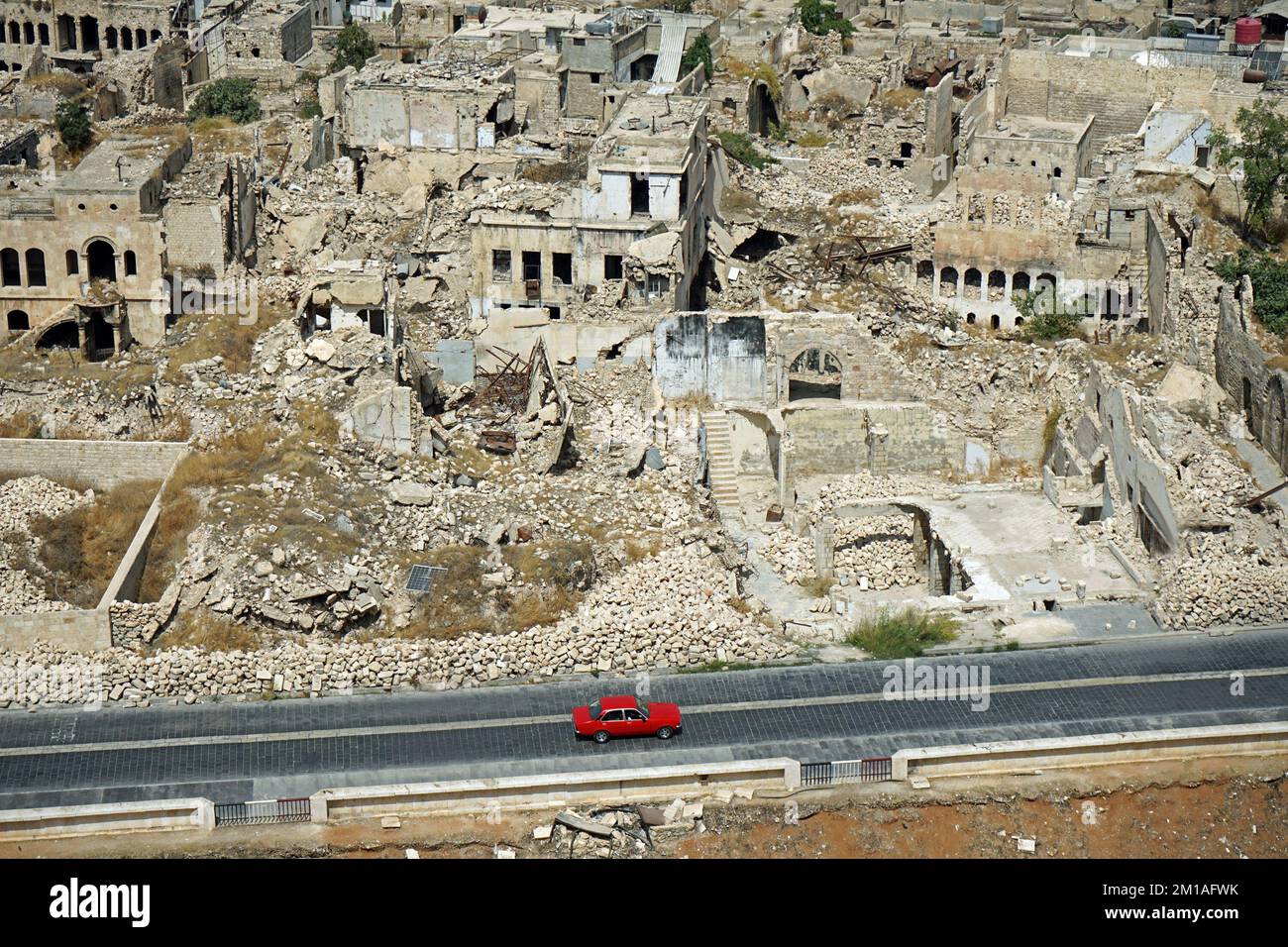 Un'auto rossa passa accanto alle rovine di un quartiere residenziale distrutto nel centro di Aleppo, Siria. Settembre 2022 Foto Stock