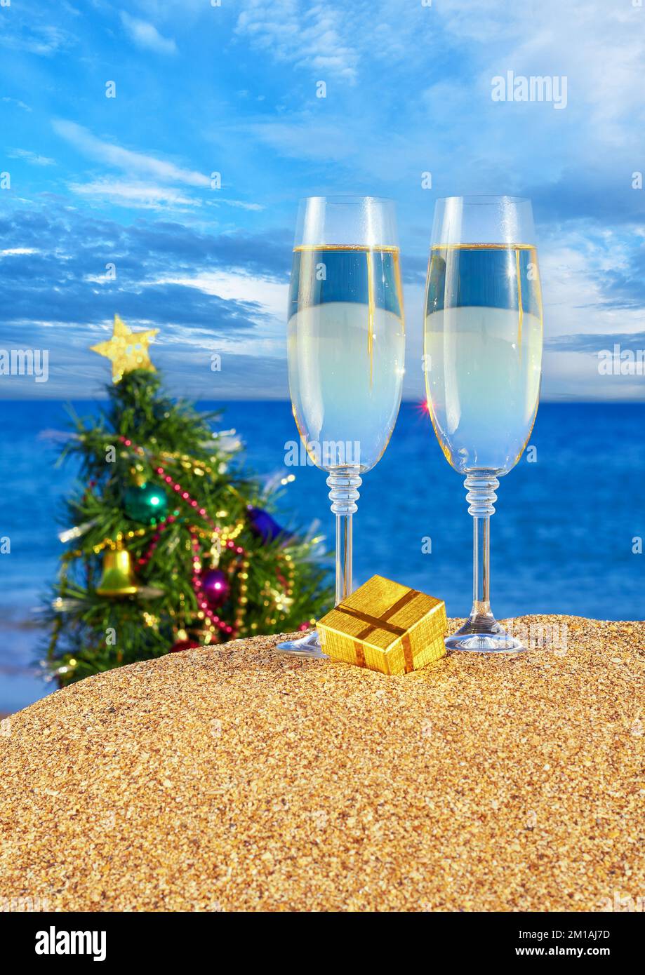 Mare con bicchieri di champagne e albero di Natale sulla spiaggia di sabbia contro il mare blu e il cielo Foto Stock