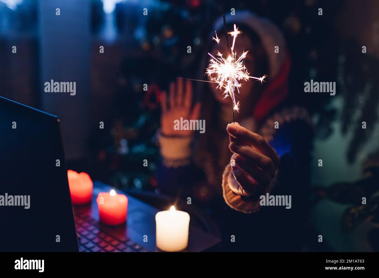 Festa di Natale online. Festeggiamo il nuovo anno a distanza utilizzando laptop e Internet. La donna brucia scintillio e candele a casa Foto Stock