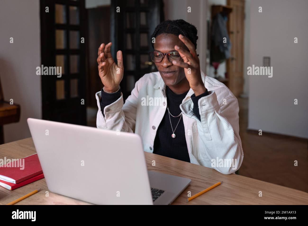 Sorridente giovane uomo africano tutor indossando auricolari wireless parlare con la webcam insegnare online da casa Foto Stock