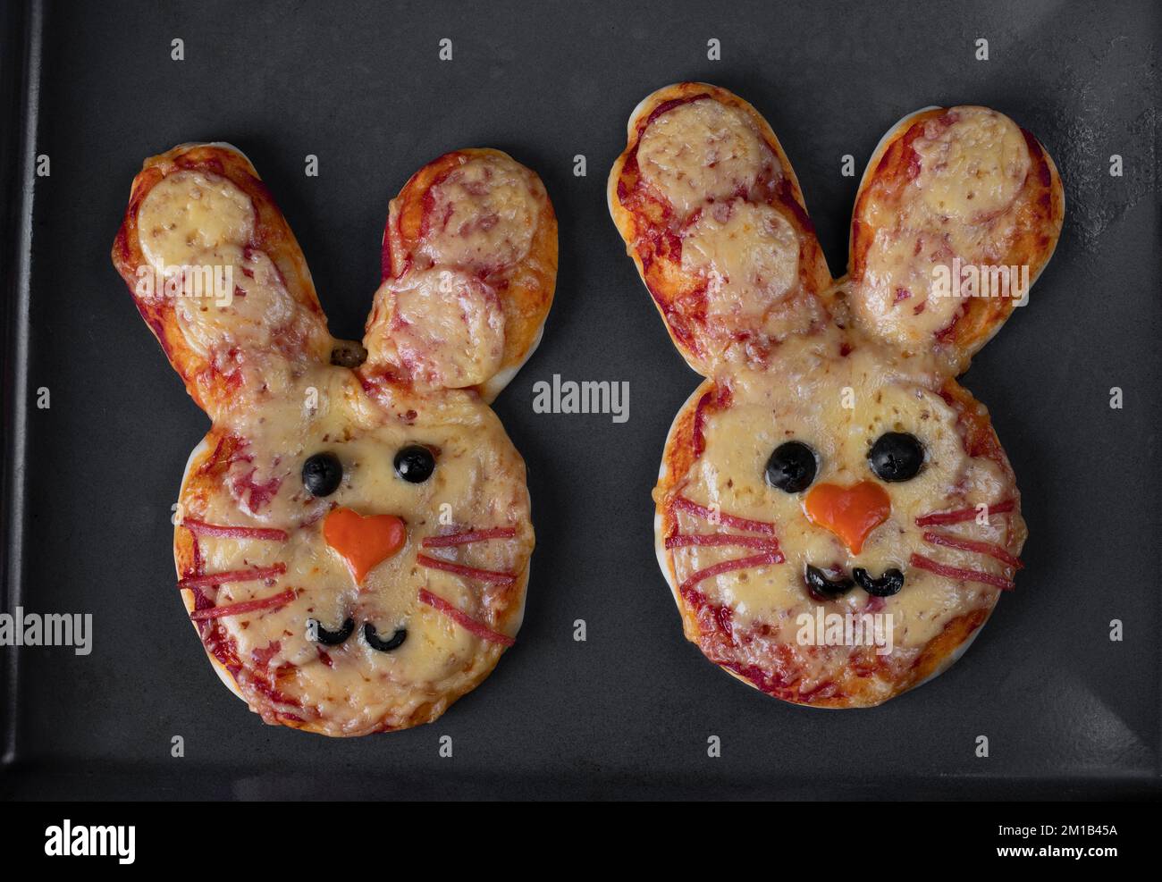 Due mini pizze al forno a forma di coniglio su foglio di cottura, l'idea di pizza fatta in casa per la festa dei bambini Foto Stock