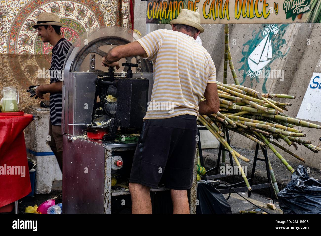 Un uomo che presea la canna da zucchero fresca sul molo di Mogan, Gran Canaria, creando una deliziosa bevanda per tutti da gustare Foto Stock