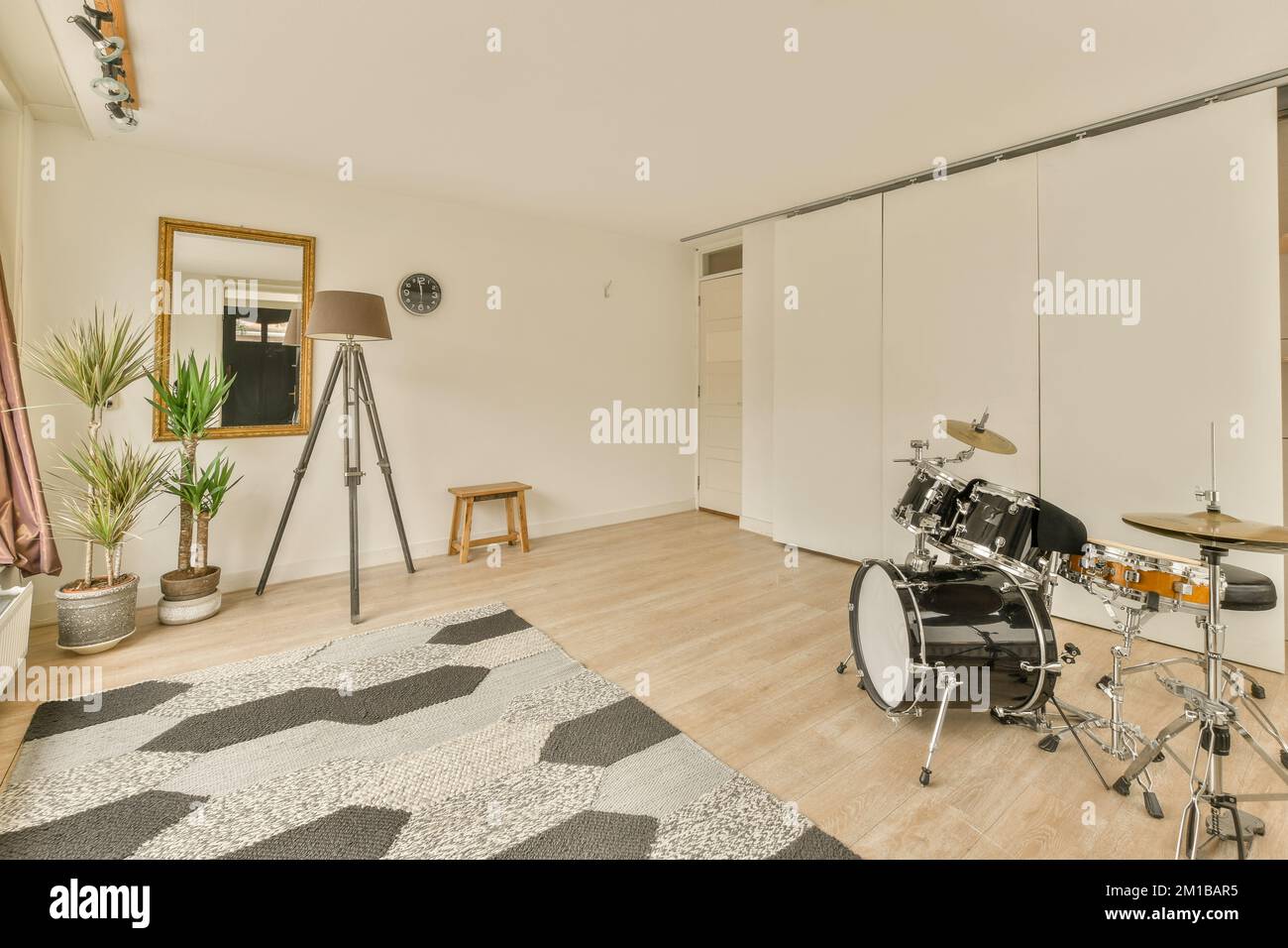 un soggiorno con un tamburo sul pavimento di fronte ad una parete bianca e pavimento in legno accanto ad un grande specchio Foto Stock