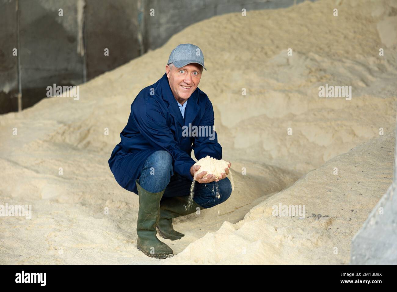 Coltivatore positivo che squatting a mucchio di farina di mais, cibo animale Foto Stock