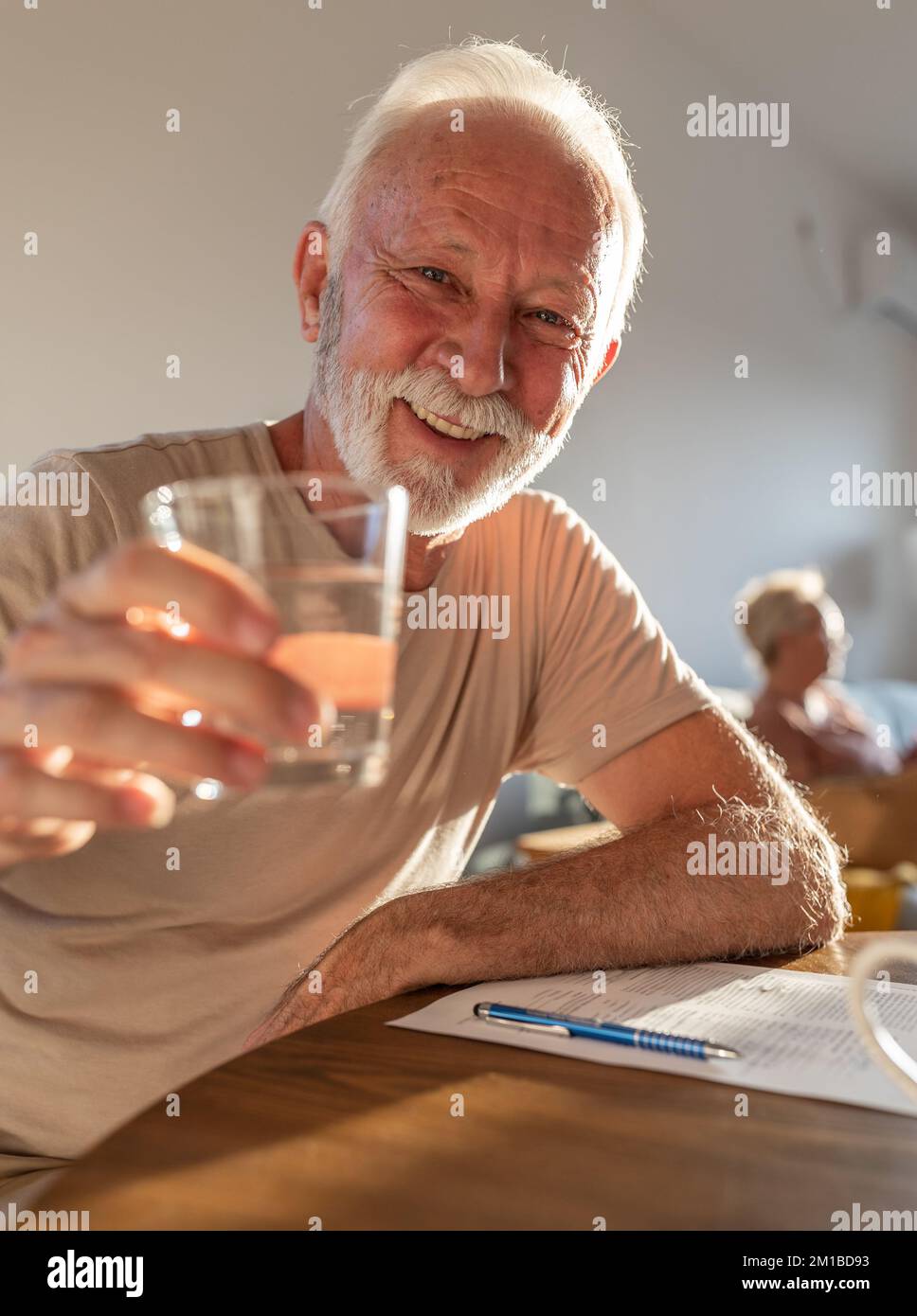 Felice uomo anziano seduto al tavolo da pranzo a casa con un bicchiere d'acqua e Grazie. Stile di vita sano nel tempo anziano concetto Foto Stock