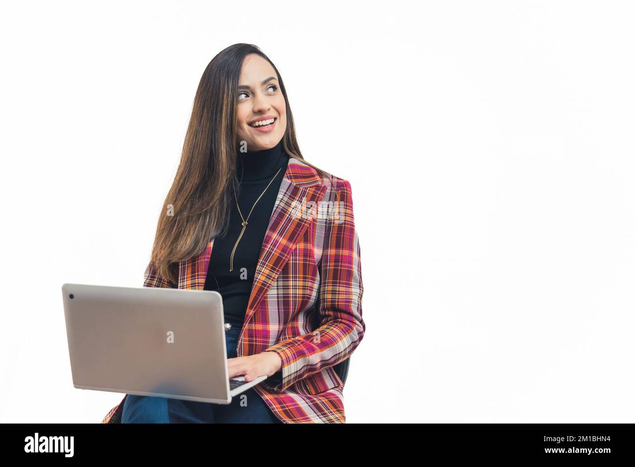 Giovane donna latinoamericana adulta vestita formaly seduta con il computer portatile sul suo grembo guardando lateralmente sorridente. Sfondo bianco copia spazio orizzontale studio shot. Foto di alta qualità Foto Stock