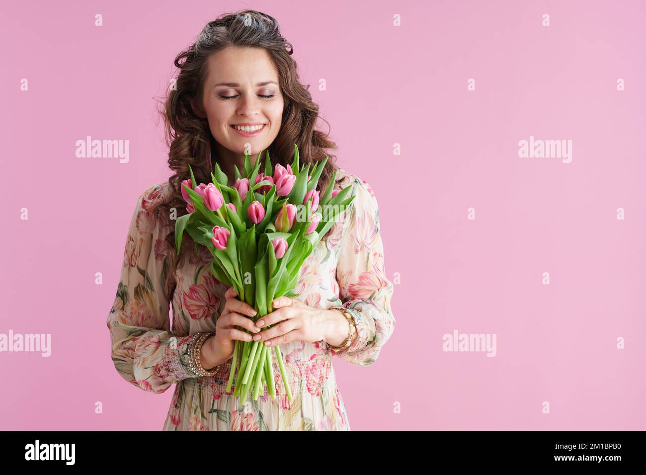 felice donna moderna con lunghi capelli di brunette ondulate con bouquet di tulipani isolato su sfondo rosa. Foto Stock