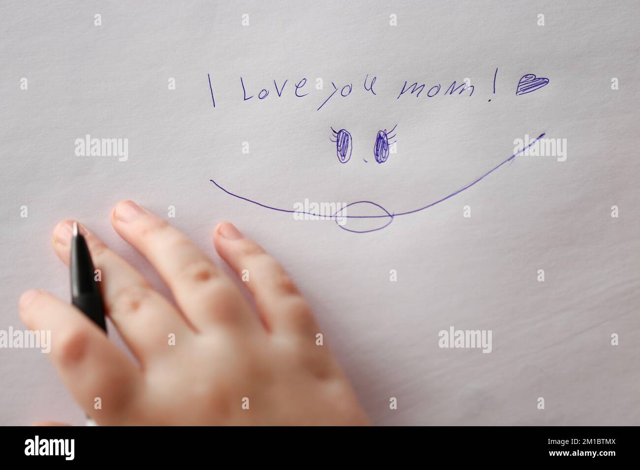 Giornata delle madri. Vi amo iscrizione mom su un foglio bianco e una mano di bambini con una pen.Holiday di tutte le madri Foto Stock