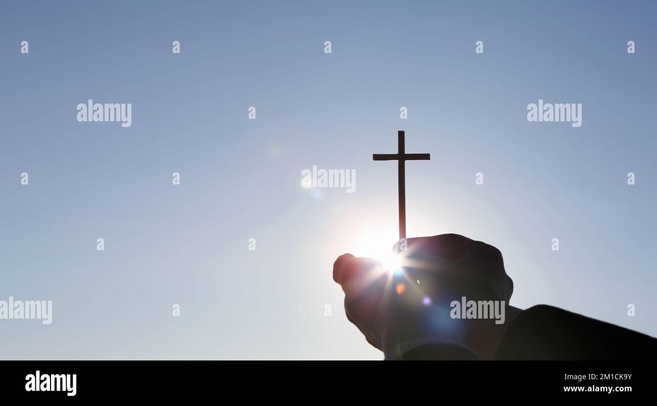 Sfondo con un sole luminoso e una Santa croce che simboleggia la morte e la risurrezione di Gesù Cristo tenuto da due mani Foto Stock