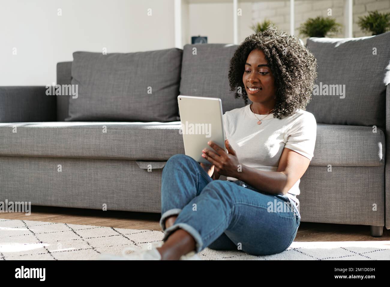 Giovane donna africana che usa un tablet digitale e sorridente mentre si riposa a casa. Foto Stock