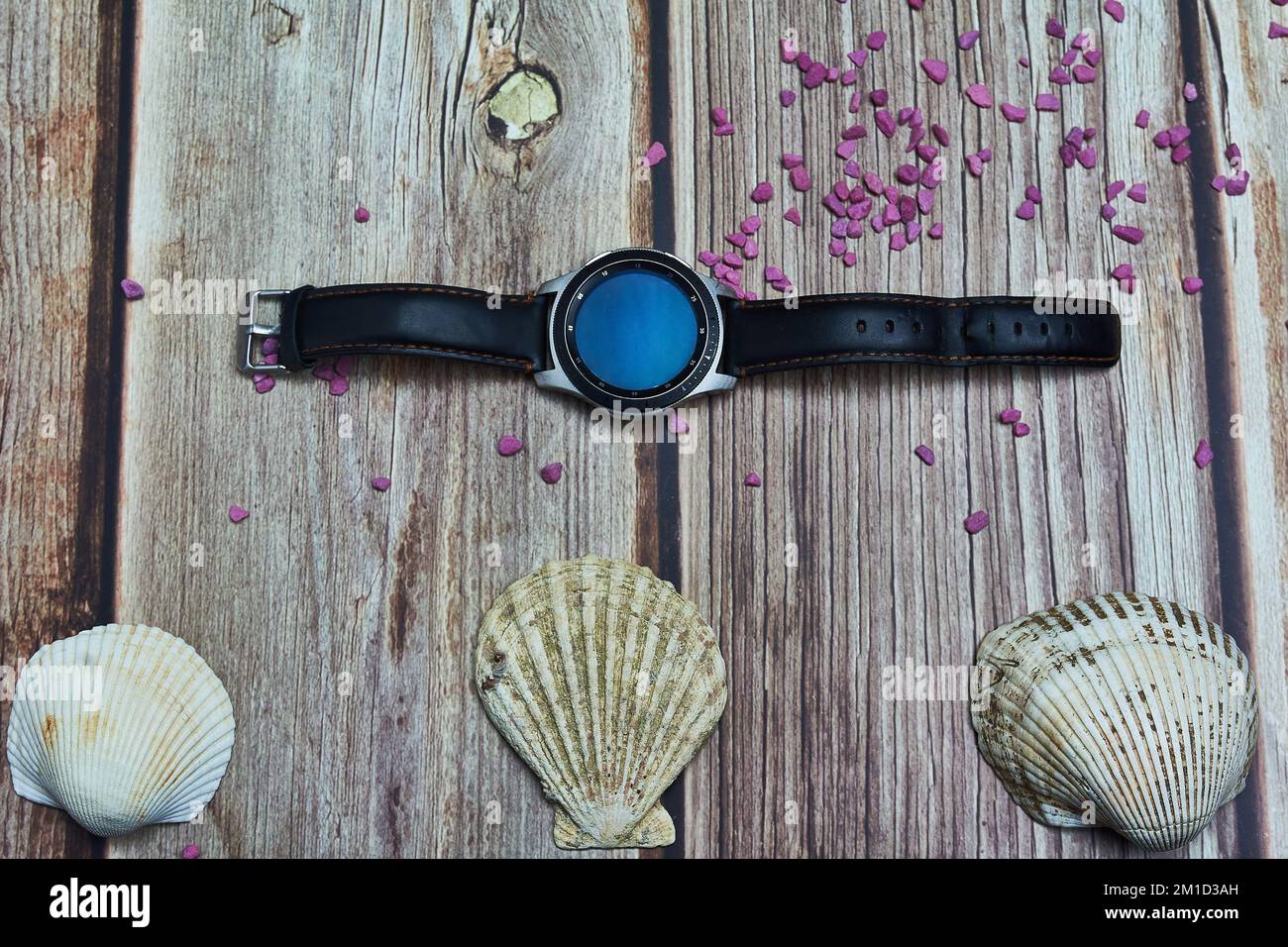 indossato smart orologio rocce viola e conchiglie di mare su legno duro Foto Stock