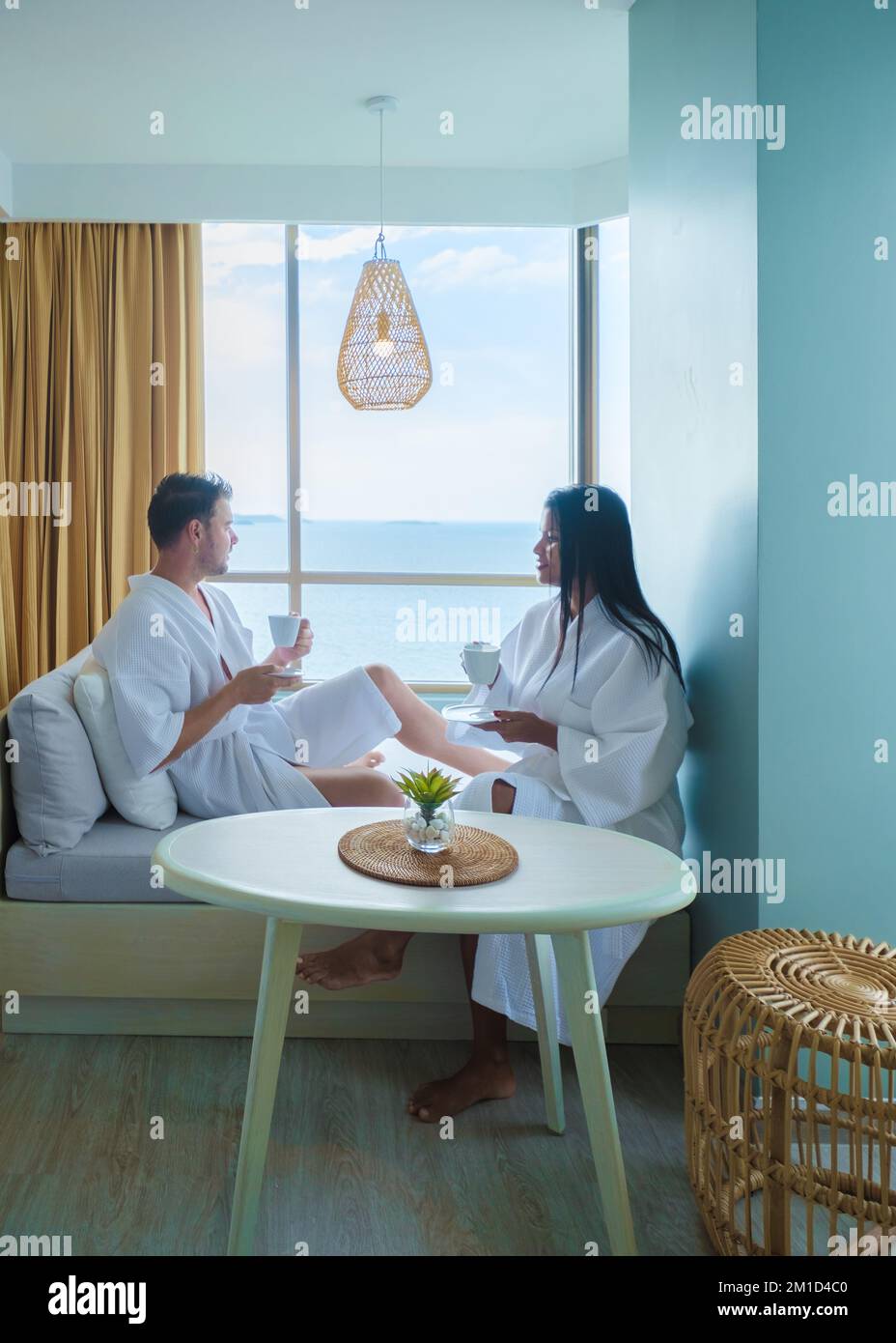 Un paio di donne asiatiche e uomini caucasici bevono caffè in una camera da letto dell'hotel che si affaccia sull'oceano in Thailandia Foto Stock
