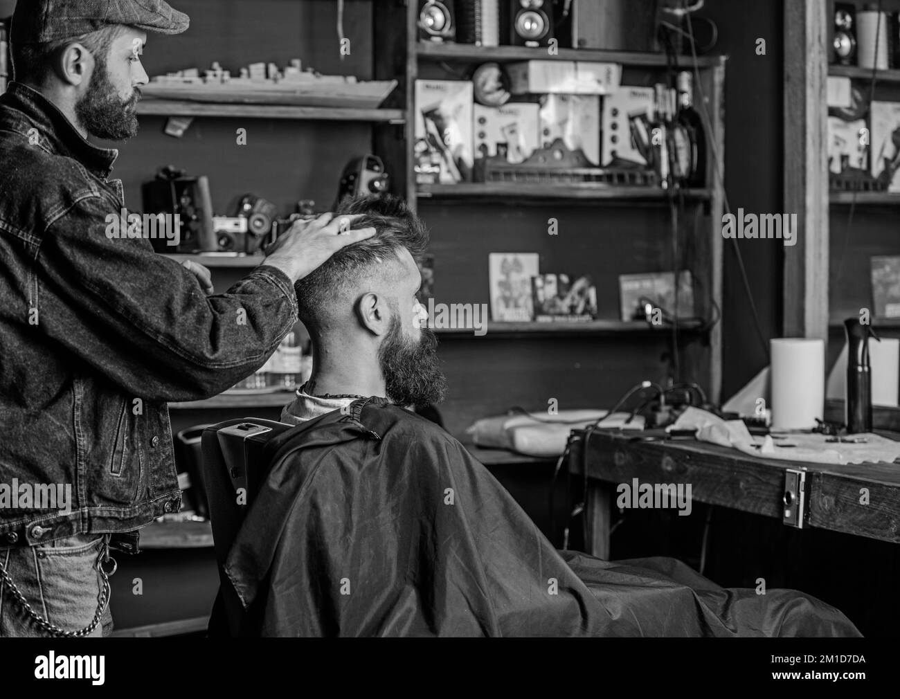 Uomo con barba e baffi in sedia da parrucchiere davanti allo specchio, mensole sullo sfondo. Barber styling capelli del cliente bearded con cera dalle mani Foto Stock