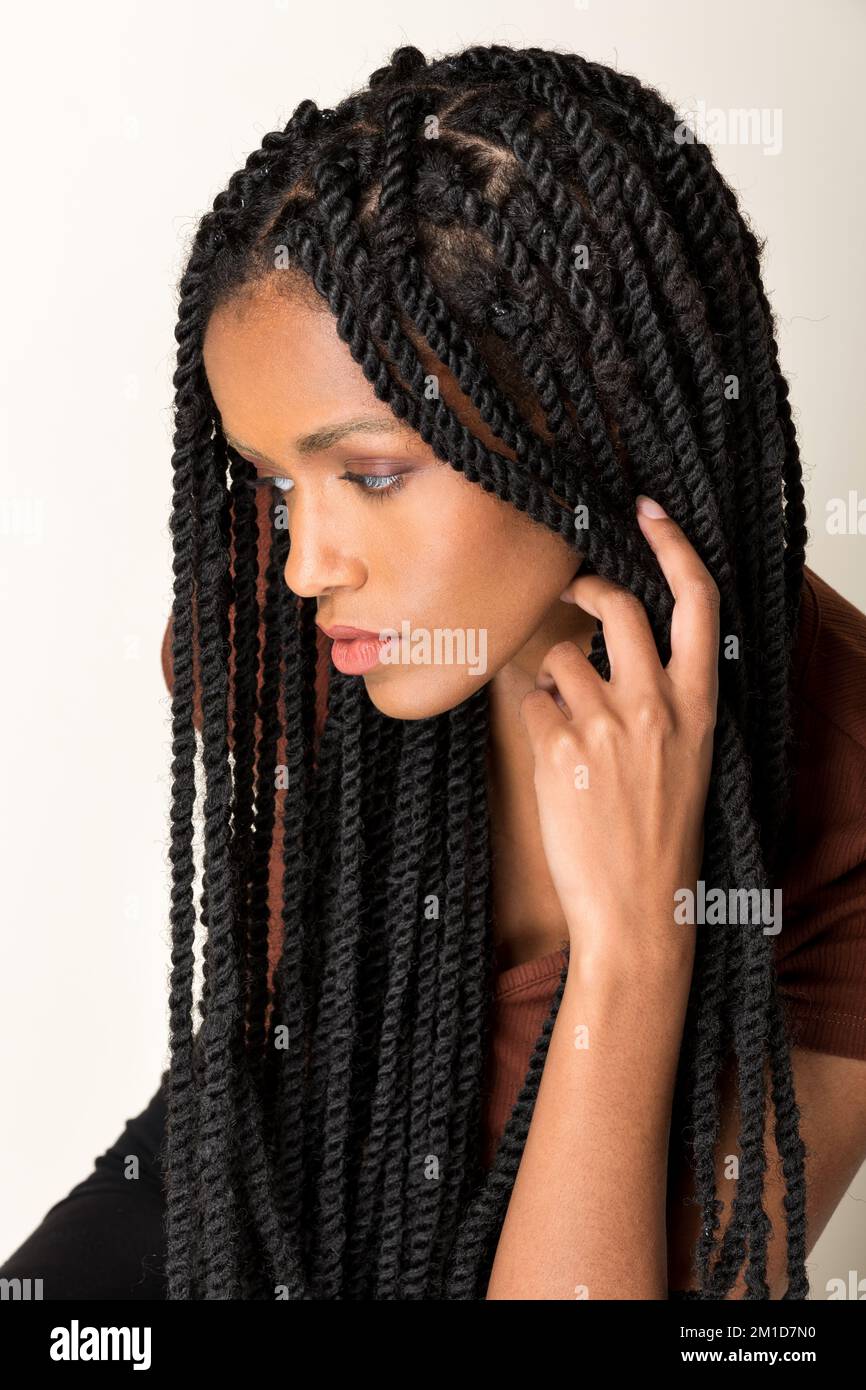 Vista laterale della giovane ragazza afro-americana con lunghe trecce afro che toccano i capelli su sfondo bianco guardando lontano Foto Stock