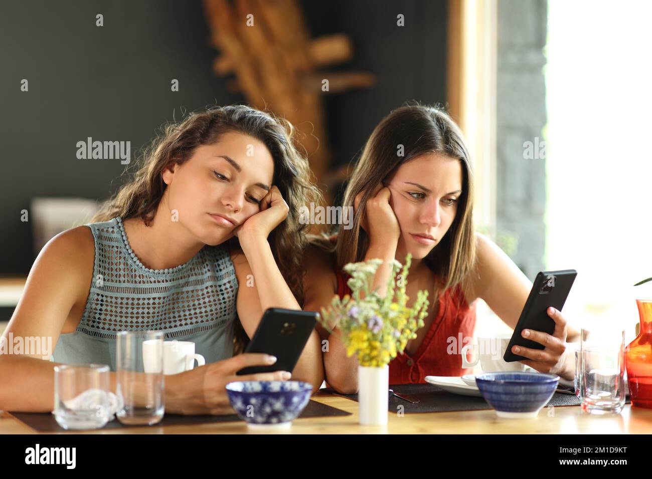 Annoiati amici che controllano gli smartphone in un ristorante Foto Stock