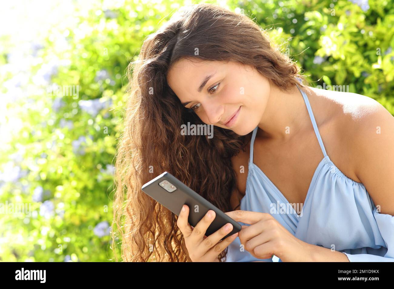 Donna felice usando il telefono delle cellule che siede in un parco Foto Stock