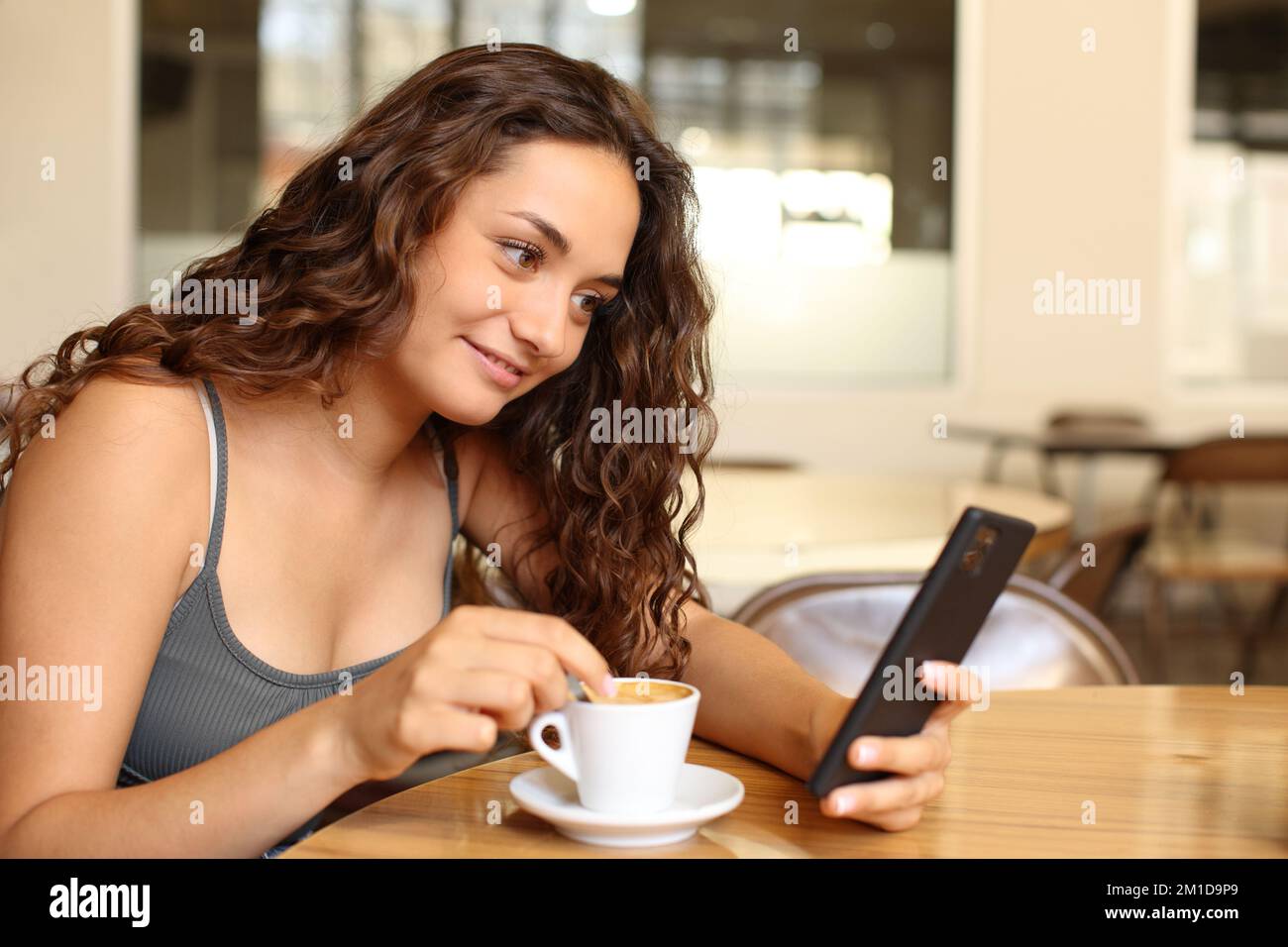 Donna che controlla lo smartphone e il caffè che mescolano seduto in un bar Foto Stock
