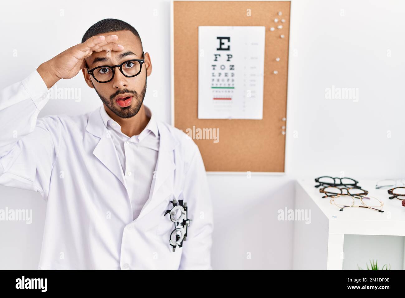 L'uomo ottico afro-americano in piedi dalla prova della vista preoccupato e sottolineato circa un problema con la mano sulla fronte, nervoso e ansioso per crisi Foto Stock