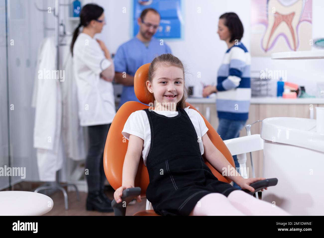 Bambina con dente mancante seduta sulla sedia in dentista ufficio sorridendo alla macchina fotografica. Bambino con la madre durante il controllo dei denti con stomatolog seduta sulla sedia. Foto Stock