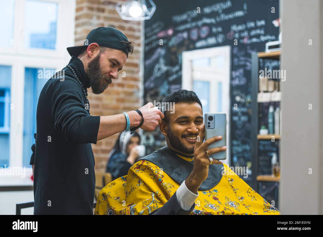 Giovane uomo che prende selfie specchio mentre ha i capelli tagliati al barbiere. Foto di alta qualità Foto Stock