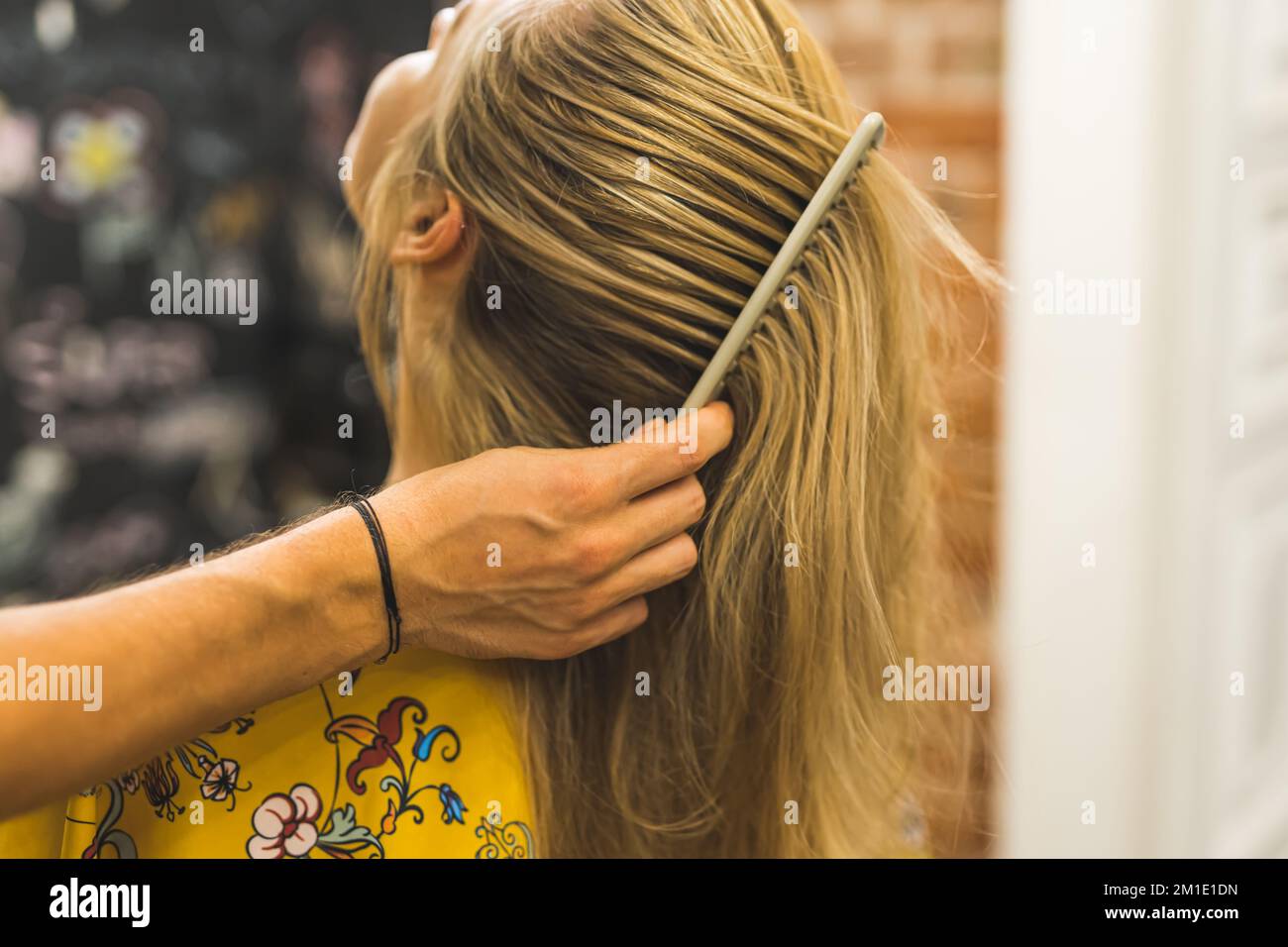 Mano di parrucchiera maschile che pettina capelli biondi lunghi di una donna . Foto di alta qualità Foto Stock