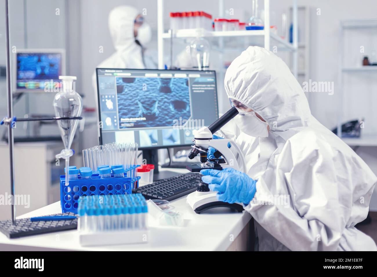Team di personale medico indossando tuta dpi facendo l'analisi del coronavirus in laboratorio moderno. Ricercatore chimico durante la pandemia globale con campione di controllo COVID-19 in laboratorio di biochimica Foto Stock