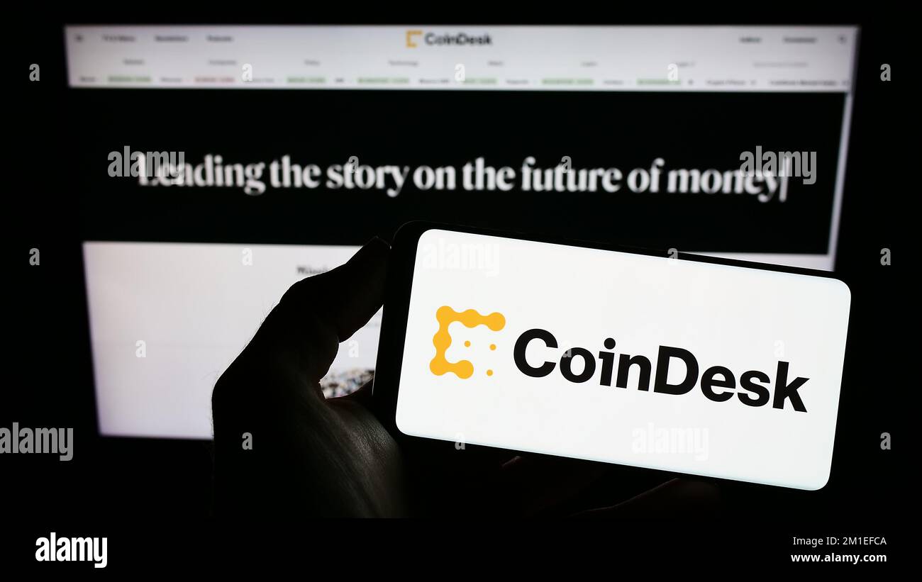 Persona che tiene in mano uno smartphone con il logo della società di notizie crittografiche statunitense CoinDesk Inc. Sullo schermo di fronte al sito Web. Messa a fuoco sul display del telefono. Foto Stock