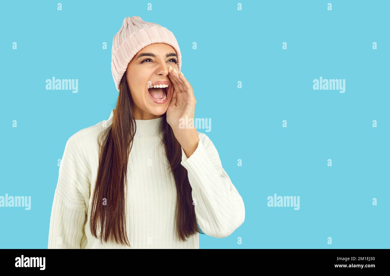 Giovane donna in abiti invernali urlare con mano in bocca su sfondo blu copia spazio Foto Stock